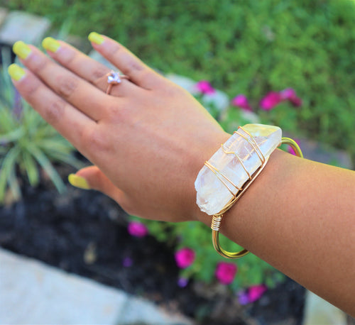 raw quartz crystal wrapped with gold wire around raw brass bracelet on women's wrist.