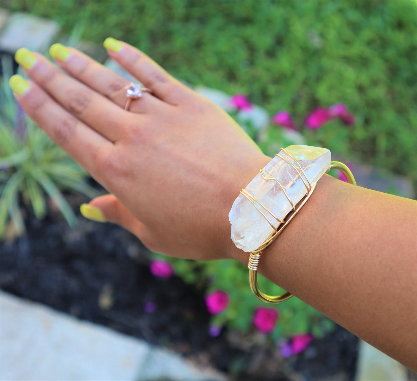 raw quartz crystal wrapped with gold wire around raw brass bracelet on women's wrist.